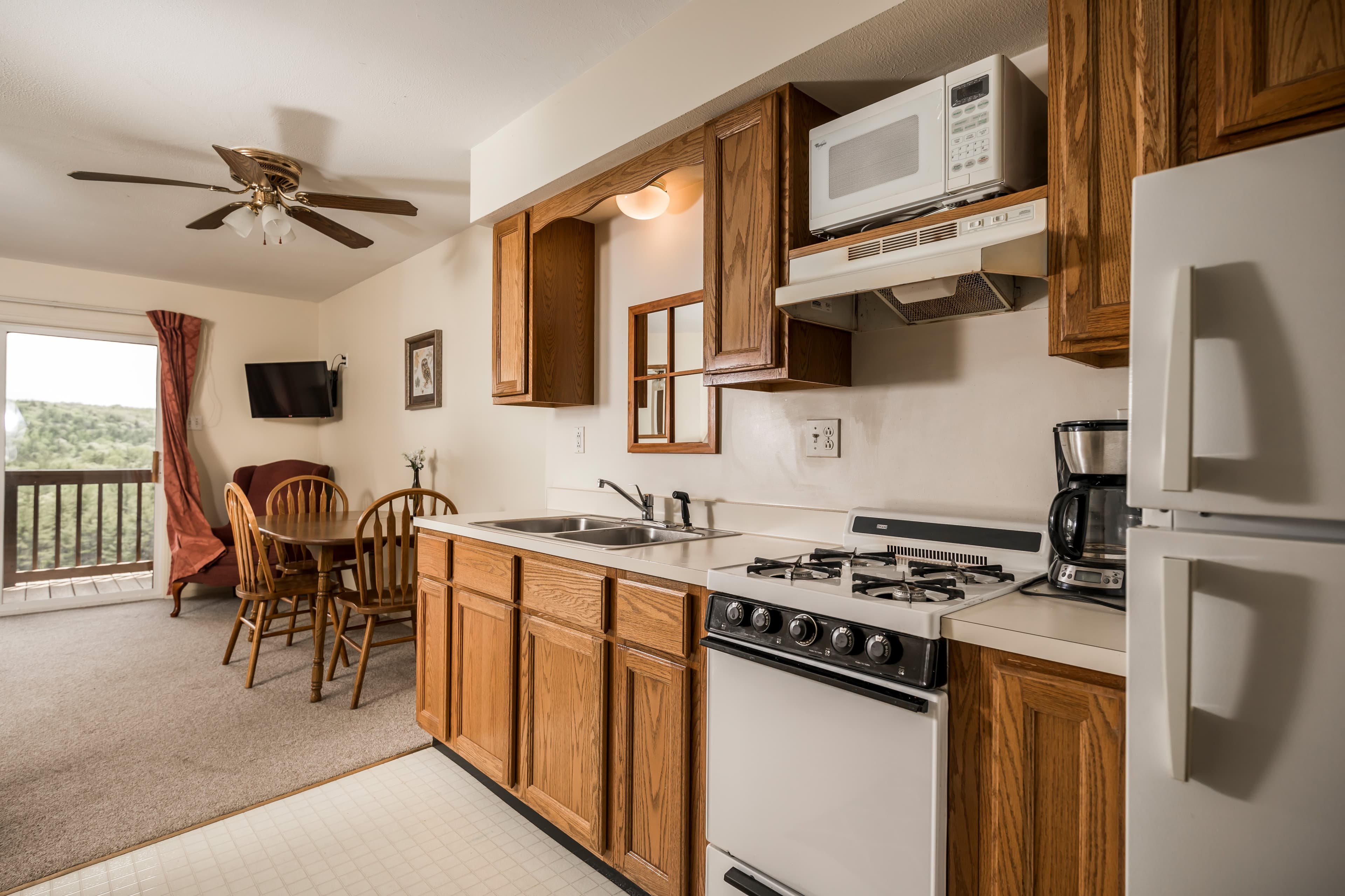 A modern kitchen with wooden cabinets, a stove, microwave, and a small dining area in the background.