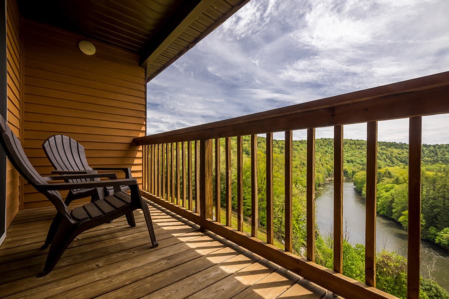 A balcony with two chairs overlooks a river and lush green trees under a partly cloudy sky.