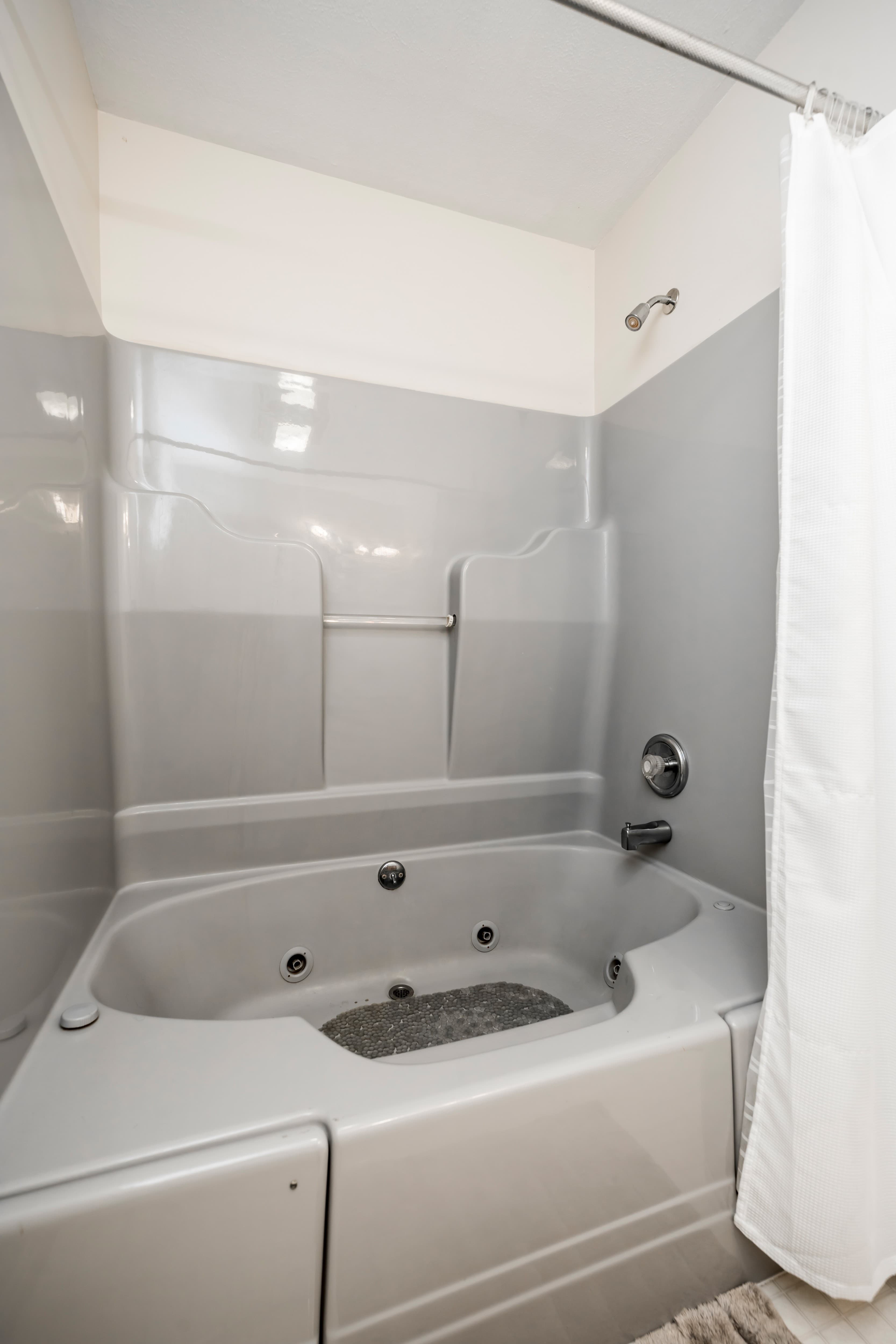 A modern gray bathtub with jets and a shower curtain.