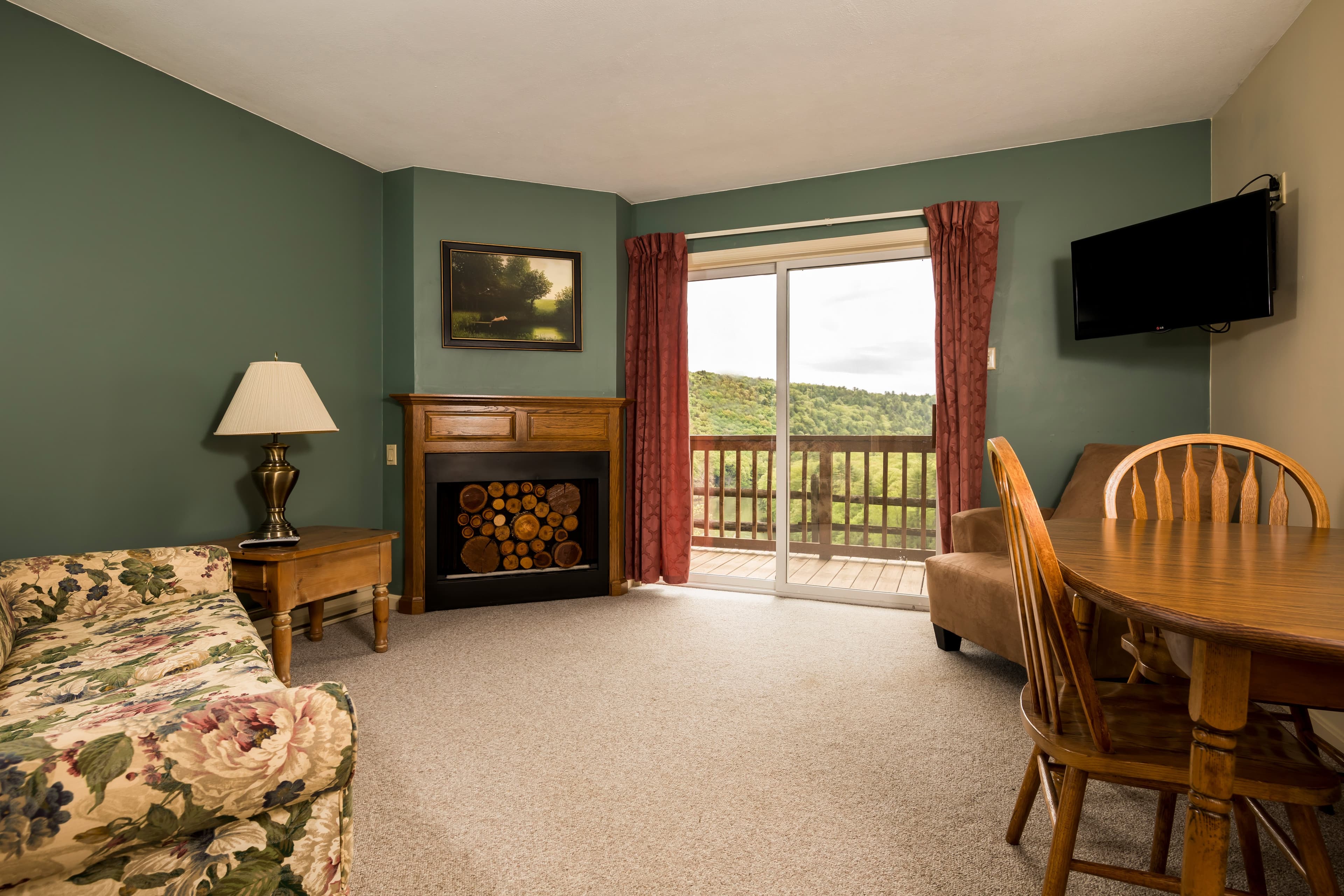 Cozy living area with a floral couch, wooden dining set, and sliding glass doors leading to a balcony.