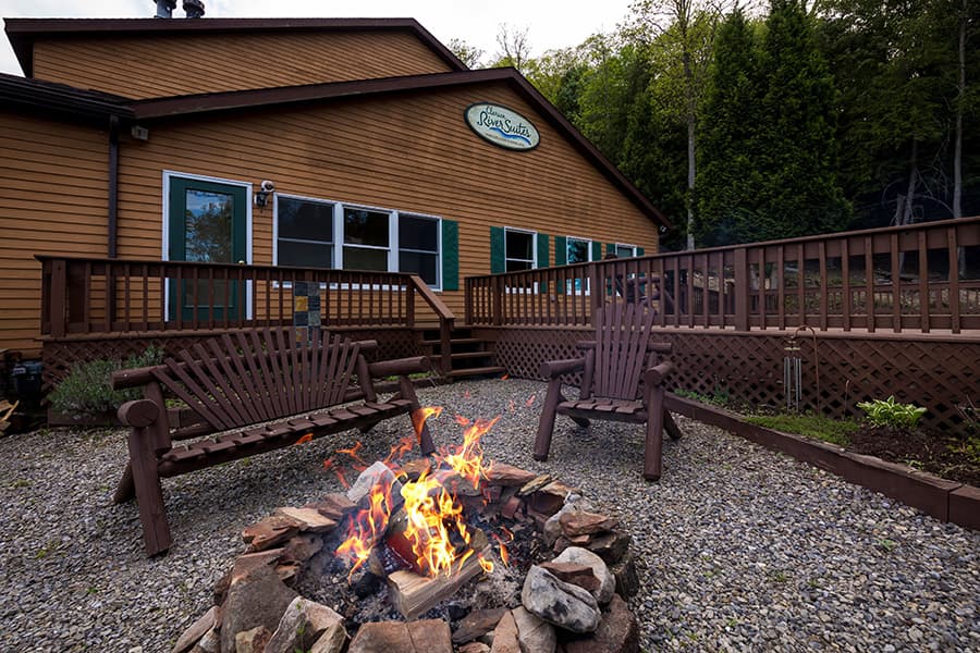 A cozy cabin exterior featuring a fire pit and wooden seating area surrounded by greenery.