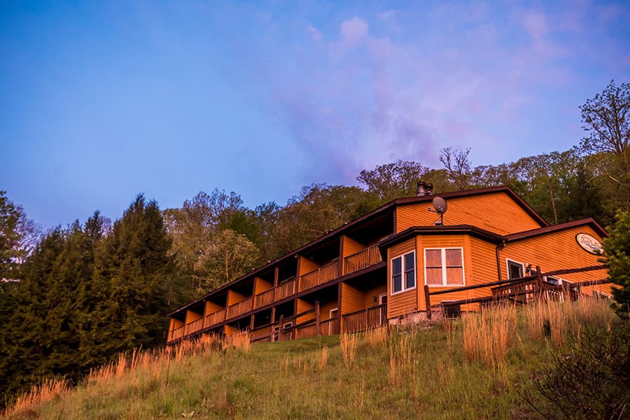 A hillside lodge with wooden siding against a colorful sky.