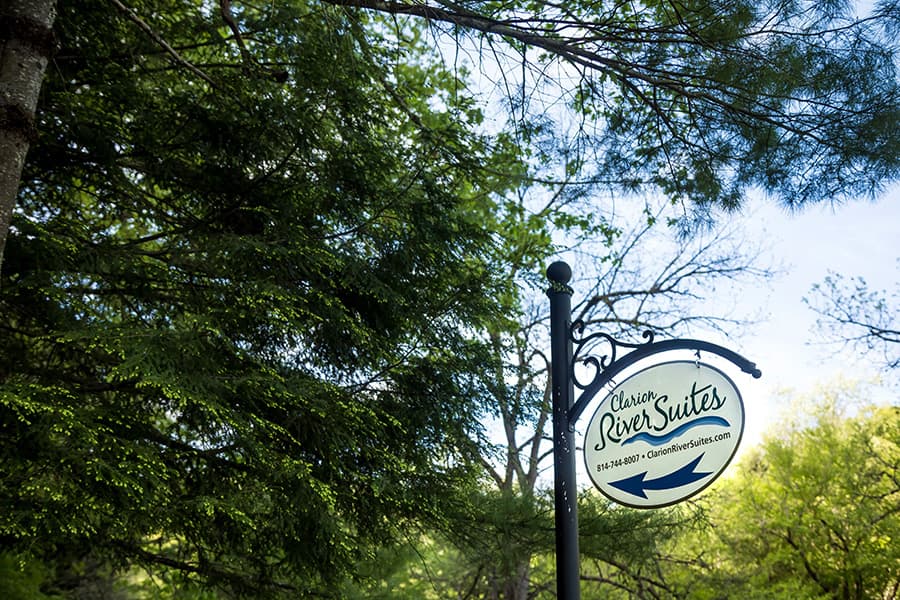 Sign for Clarion River Suites amidst green foliage.