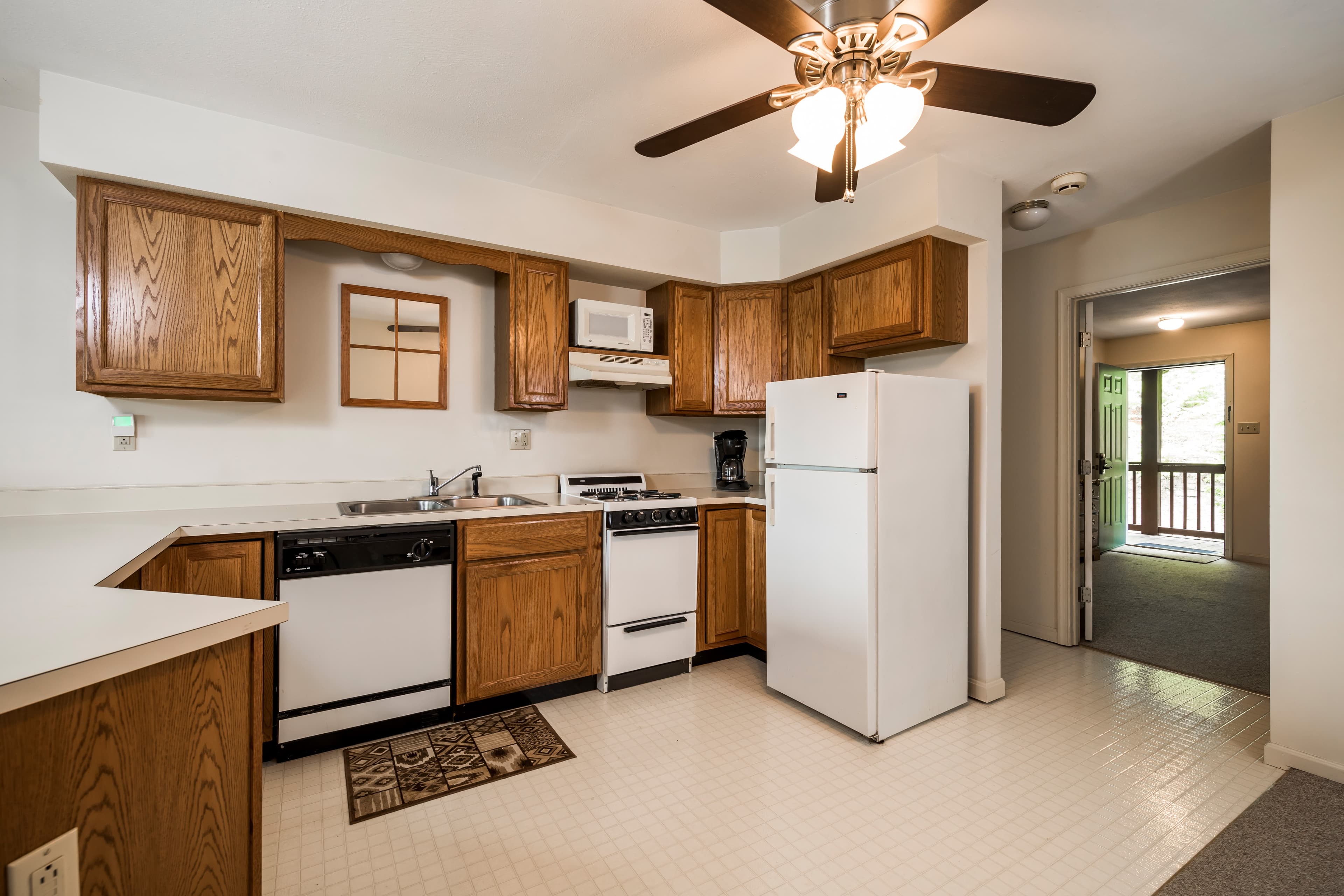 A modern kitchen with wooden cabinets, white appliances, and a door leading to an outdoor balcony.