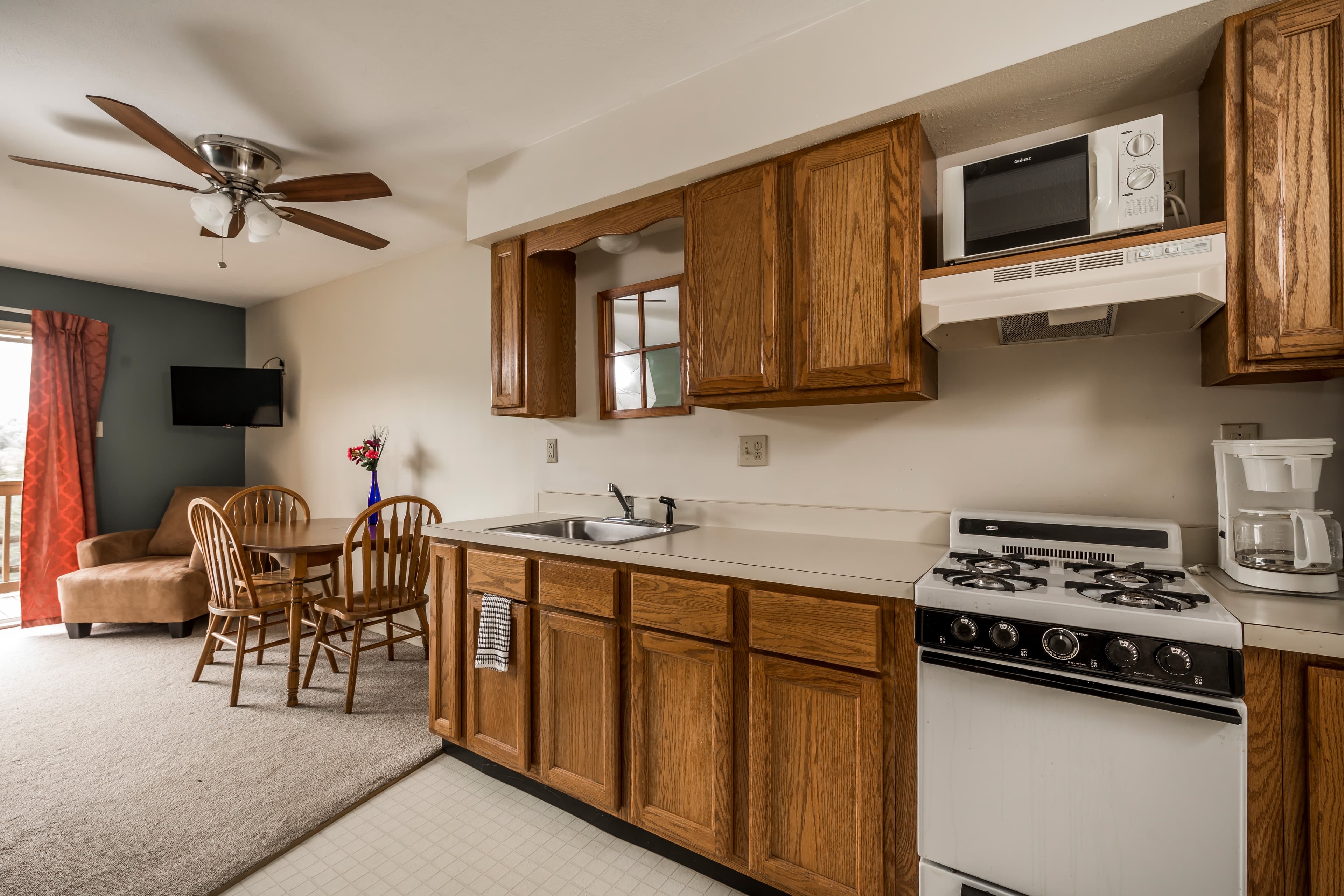 A compact kitchen featuring wooden cabinetry, a stove, microwave, and a small dining area with a table and chairs.