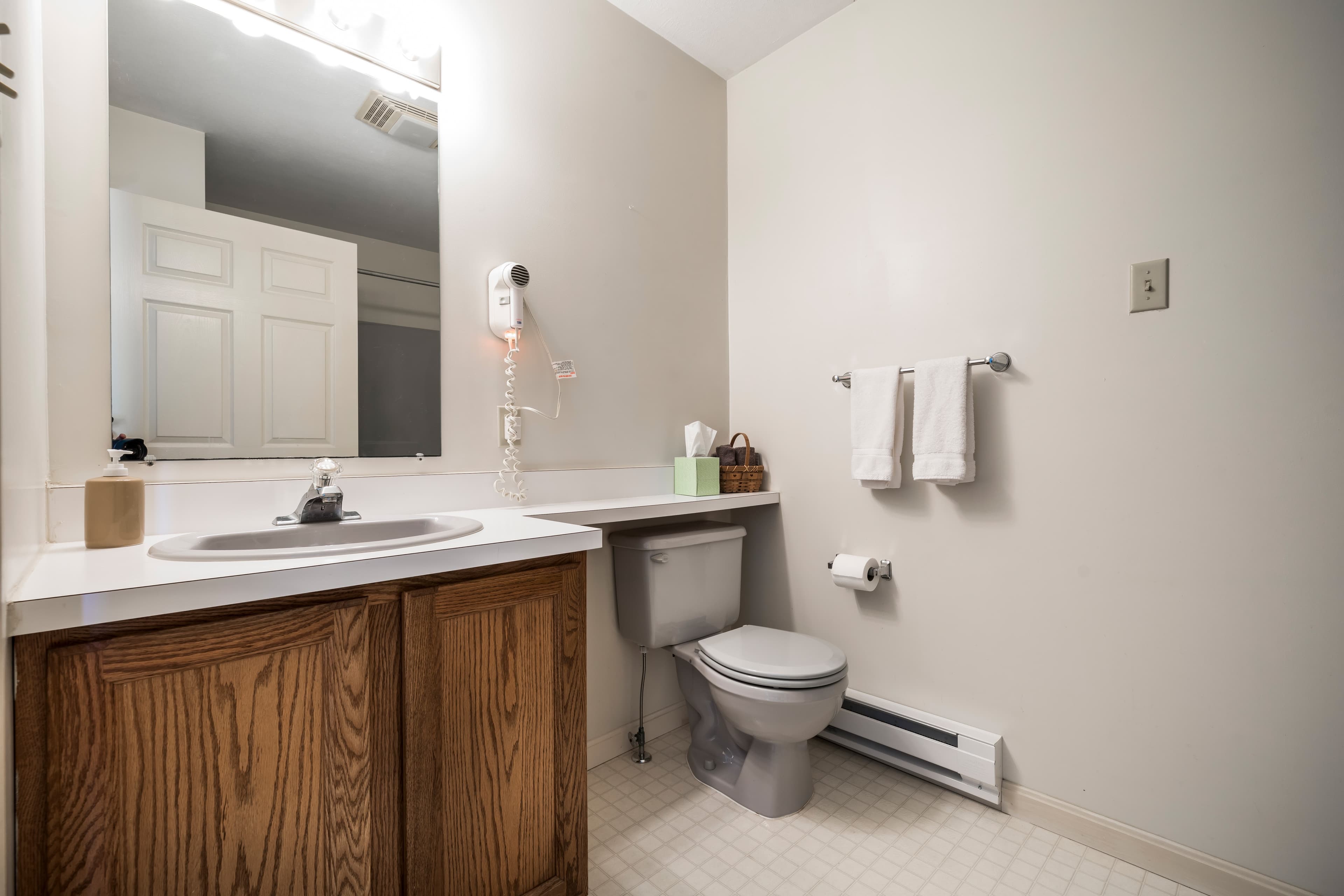 A simple, modern bathroom featuring a sink, mirror, toilet, and towels on a rack.